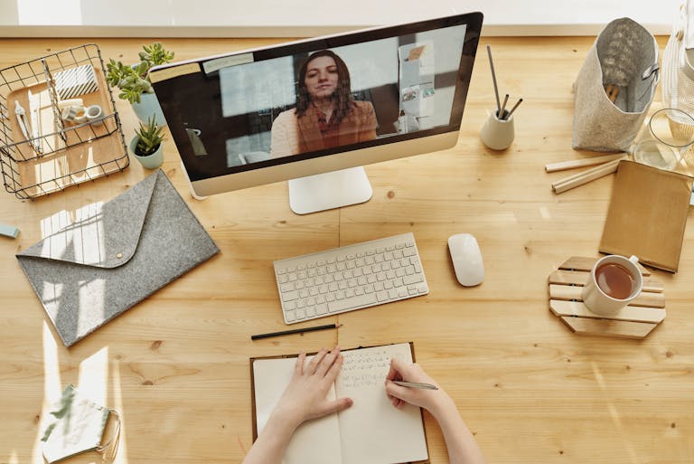 TestEvent Person taking notes during a video call at a neatly organized home desk, showing remote work lifestyle.