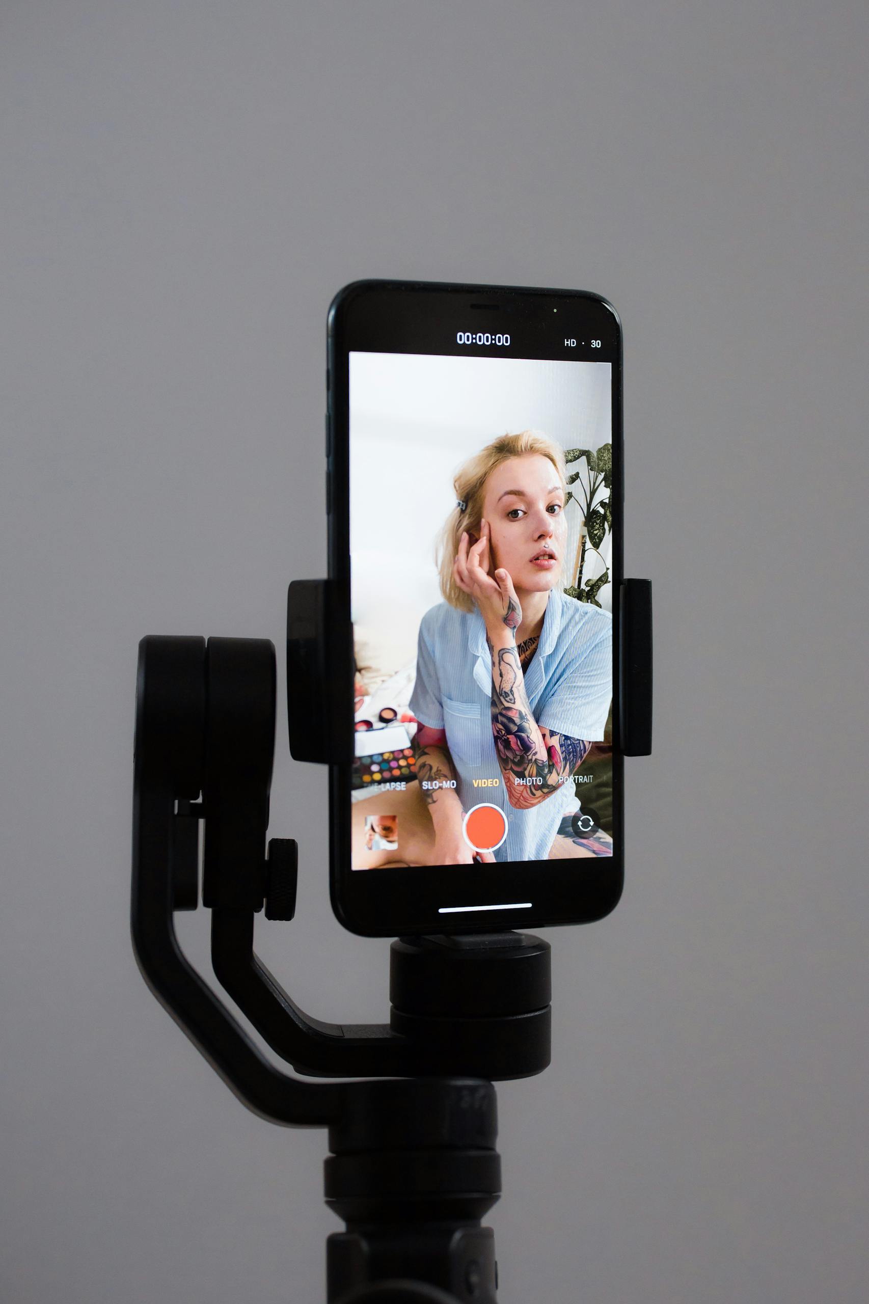 Woman filming a vlog using a smartphone on a tripod, demonstrating a makeup tutorial.